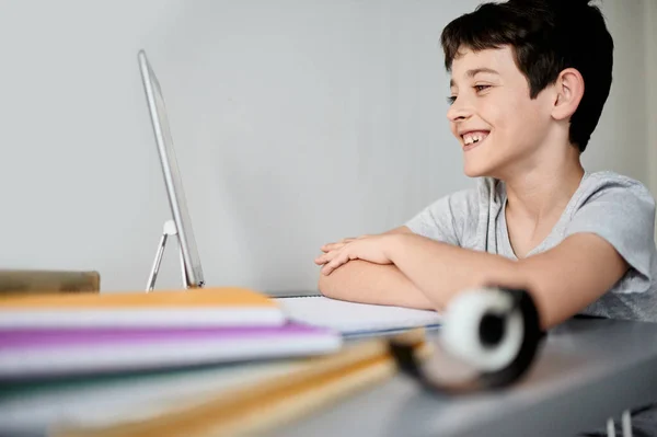 Χαρούμενο αγοράκι που γράφει στο σημειωματάριο. Παιδί κάθεται στο γραφείο σπίτι και κάνει τα μαθήματά του. Σχολείο, παιδιά, εκπαιδευτική έννοια — Φωτογραφία Αρχείου