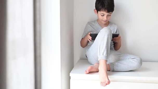 Um rapaz a jogar tablet depois de fazer os trabalhos de casa. Atirador em casa. Distância social durante a quarentena . — Vídeo de Stock