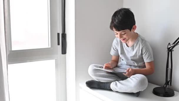 Un ragazzo che gioca a tablet dopo aver fatto i compiti. Sparatutto in casa. Distanza sociale durante la quarantena . — Video Stock