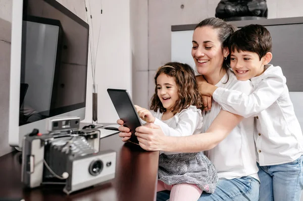 Çocuklarıyla orta yaşlı bir anne çalışma alanında dijital tablet kullanıyor.