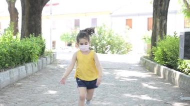 Parkta maskeyle koşan küçük bir kız.