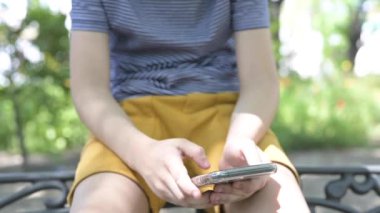 Parkta akıllı telefonla oynayan bir çocuk. Dijital bağımlılık. Koronavirüse karşı koruyucu maskeli çocuk.