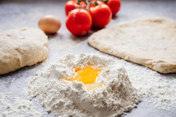 Soyut taştan bir arka planda, domates, un, peynir ve yumurta gibi malzemelerle yapılan ev yapımı pizza için hamur topu.