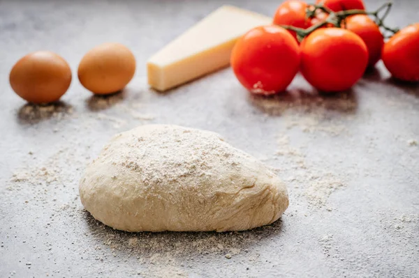 Soyut taştan bir arka planda, domates, un, peynir ve yumurta gibi malzemelerle yapılan ev yapımı pizza için hamur topu.