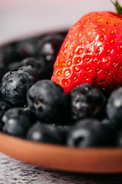 Rustic handmade plate full of blueberries with a strawberry on top ready to eat placed on a cement textured background and pink background — Stock Photo, Image