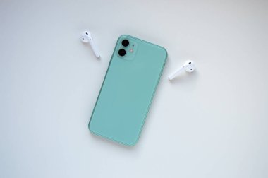 Beyaz arka planda iki kablosuz kulaklığı olan modern, naneli bir akıllı telefon. Modern ve minimalist kavram.