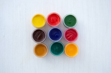 Gouache kavanozlarda resim yapıyor. Parlak renk. Kırmızı, pembe, sarı, turuncu, mavi ve yeşil renkler küçük kavanozlarda. Yukarıdan manzara. Düz yatıyordu