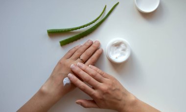 Aloe suyu ile el bakım kremi. Beyaz arka planda eller, krem ve aloe yaprakları. Yukarıdan görünüşü.
