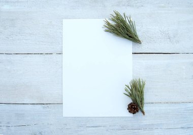 Beyaz ahşap bir masa arkasında boş bir kağıt ve çam dalları olan bir kadın masaüstü düzeni. Boşluk. Stylize edilmiş stok fotoğrafı, web afişi. Düz yatış, üst görünüm.