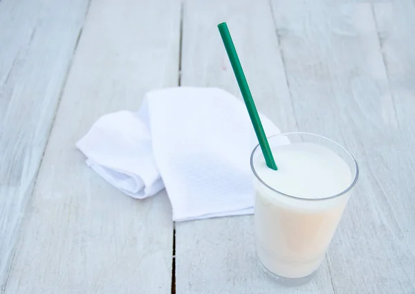 Bir bardak kefir ya da beyaz ahşap arka planda yeşil pipetli ayran. Probiyotiklerle mayalanmış süt ürünü. Vücudunuzu ve diyetinizi korumak için faydalı bir içecek..