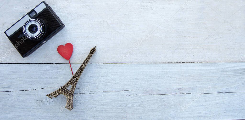 Travel and romantic concept. Retro camera and statuette of the Eiffel tower with mini heart on a white wooden background. Top view. Flat lay. Mock up. Copy space.