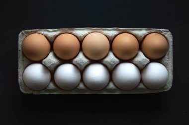 Karanlık bir arka planda karton bir kutuda on yumurta. Üst üste 5 beyaz ve 5 kahverengi yumurta. Üst görünüm.