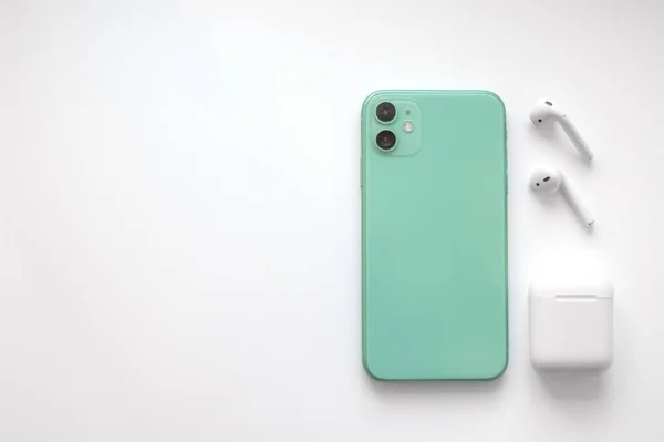 Beyaz arka planda iki kablosuz kulaklığı olan modern, naneli bir akıllı telefon. Modern ve minimalist kavram.