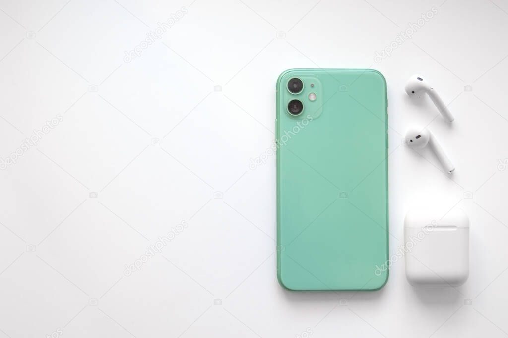 A modern mint-colored smartphone with two wireless headphones on a white background. Modern and minimalistic concept.