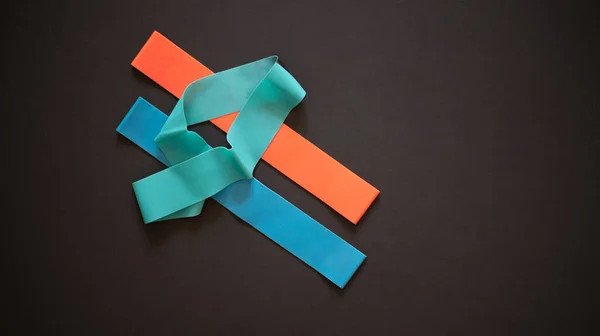 Multi-colored elastic rubber bands for fitness on a black background. A set of rubber bands of different colors - red, blue and turquoise. Ideal for training at home.