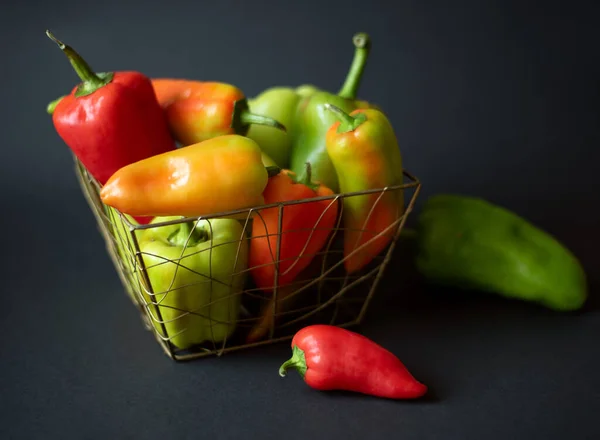 A large bowl of fresh bell peppers of different sizes and colors on a black background.
