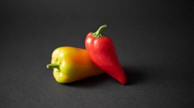 İki taze dolmalık biber. Arka planda, bahçeden farklı renkte ve şekilde. Siyah arka planda kırmızı ve sarı dolma biber..