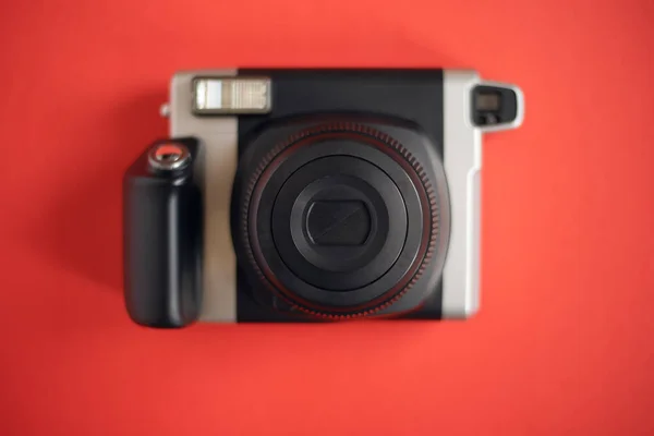 A modern black instant print camera on a bright red background.
