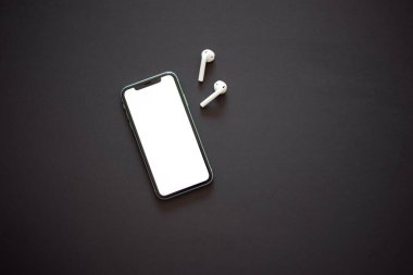 Beyaz ekranlı modern akıllı telefon ve siyah arka planda iki beyaz kablosuz kulaklık. Modern ve minimalist kavram.