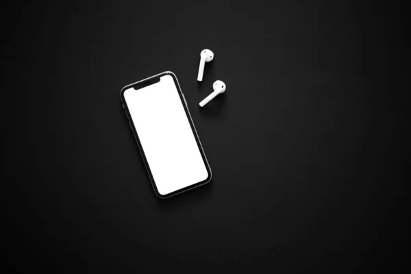 Beyaz ekranlı modern akıllı telefon ve siyah arka planda iki beyaz kablosuz kulaklık. Modern ve minimalist kavram.