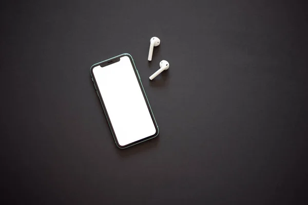 Beyaz ekranlı modern akıllı telefon ve siyah arka planda iki beyaz kablosuz kulaklık. Modern ve minimalist kavram.