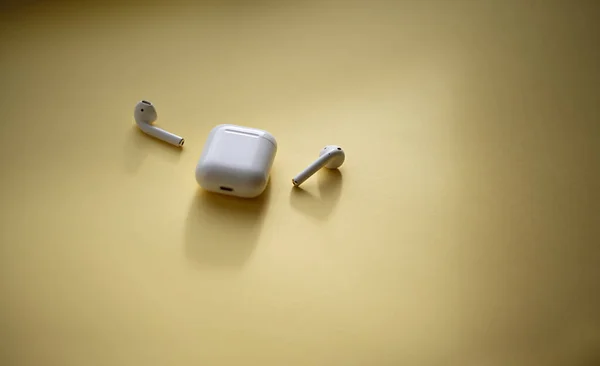 Beyaz kablosuz kulaklıklar ve parlak sarı arka planda bir kulaklık kutusu. Modern kablosuz bluetooth kulaklık ve şarj çantası.