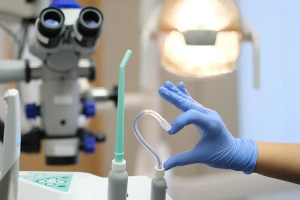 Hand in Blue latex glove and saliva ejector in shape of heart and dental microscope on beckground