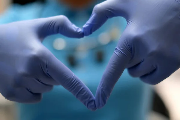 Mains d'infirmière en gants de latex bleu en forme de cœur sur le fond de son corps en chemise bleue — Photo