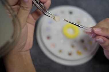Diş teknisyeni cımbız kullanarak dişlere seramik malzeme uygular ve diş macunu arkaplanını fırçalar. Diş teknolojisi yakın plan.