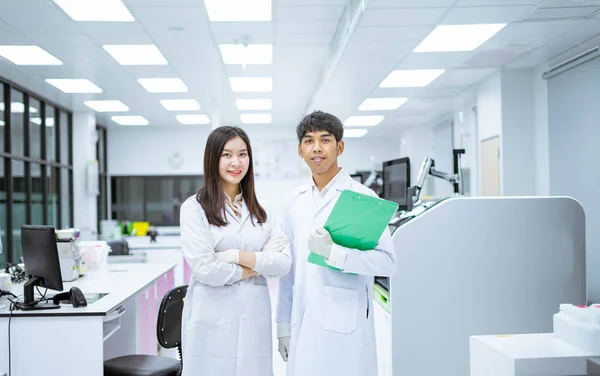 Dwóch Młodych Uśmiechniętych Naukowców Białym Fartuchu Laboratoryjnym Stojących Automatycznym Analizatorem — Zdjęcie stockowe
