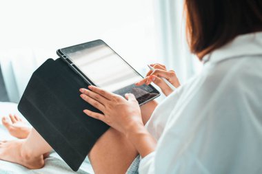 Yatak odasında otururken tablet bilgisayarda çalışan genç bir kadın. ev kavramından çalışma