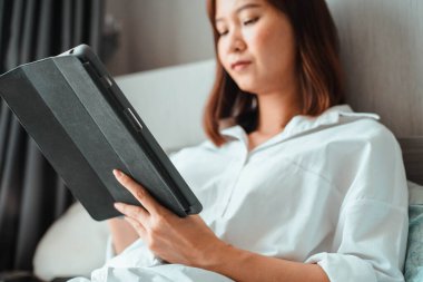 Yatak odasında otururken tablet bilgisayarda çalışan genç bir kadın. ev kavramından çalışma