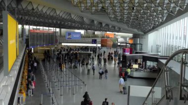 Kamera en üst kattan zemin kata açıyla çekilmiş. Terminal binasından hızla geçen yolcuları gösteriyor..