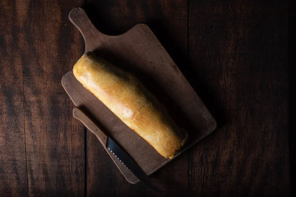 Homemade bread stuffed with shredded chicken on rustic wood and knife with black background, Top view.