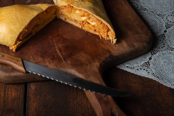 Homemade bread stuffed with shredded chicken on rustic wood and knife with black background, selective focus.
