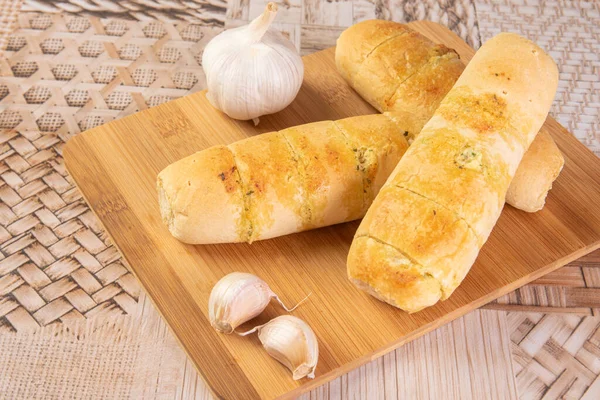 Garlic bread stuffed with cheese arranged on a cutting board with garlic around it, on a table, selective focus.
