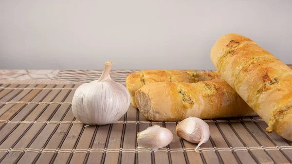 Garlic bread stuffed with cheese arranged on a bamboo mat with garlic around it on a table, selective focus.