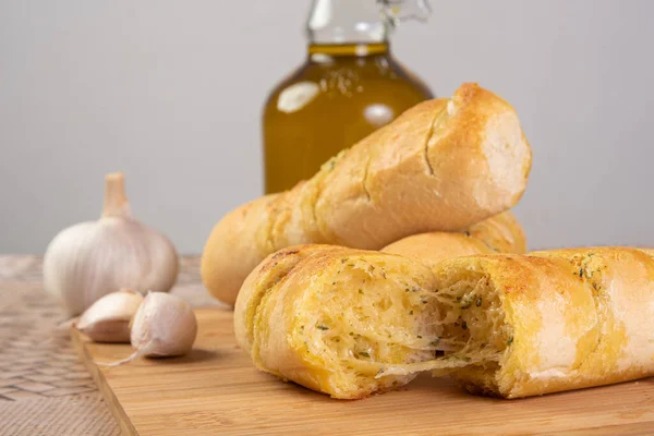 Garlic bread stuffed with cheese arranged on a cutting board with garlic around it and a bottle of olive oil on a table, selective focus.