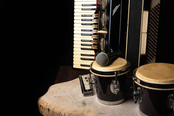 Old accordion, harmonica, bong and microphone on a rustic wooden surface with black background and low key lighting, selective focus.