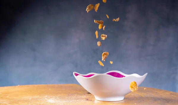 Breakfast cereal, corn flakes falling into a bowl on rustic wood, blue background, selective focus.