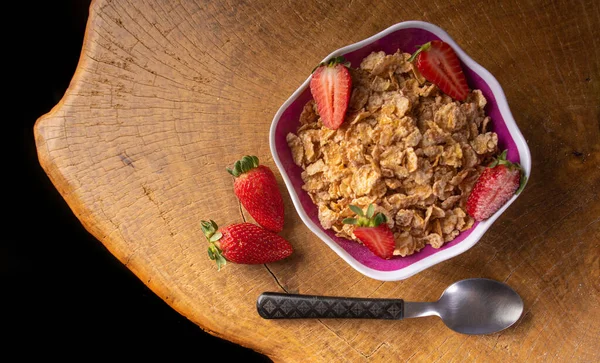 Breakfast cereal, corn flakes, strawberries in a bowl on rustic wood, Top view.