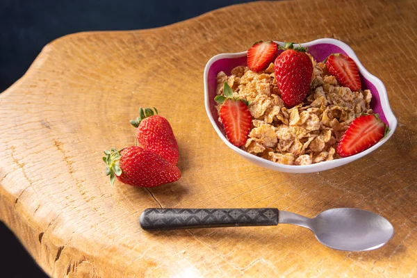 Breakfast cereal, corn flakes, strawberries in a bowl on rustic wood, selective focus.