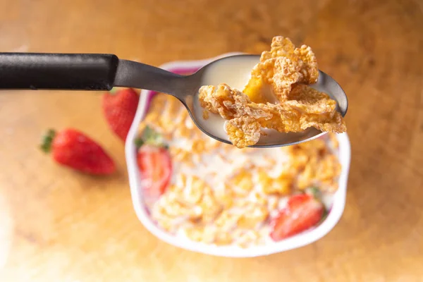 Breakfast cereal, corn flakes, strawberries and milk, in the foreground a spoon with corn flakes and milk. selective focus.