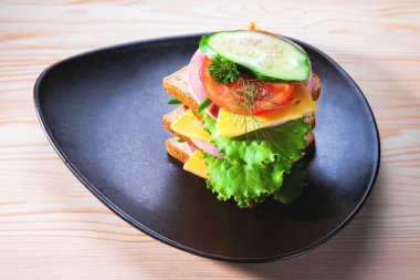 Sosisli ve peynirli sandviç, otlar, domates ve salatalık, üçgen şeklinde koyu bir tabakta. Öğlen bir şeyler atıştır. Seninle bir sandviç. Kahvaltı ya da öğle yemeği için kadeh kaldıralım.