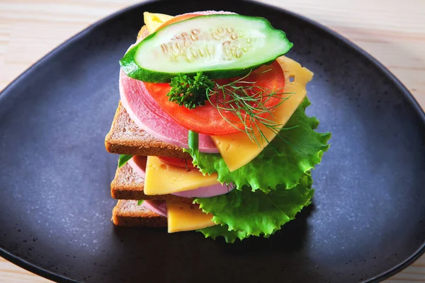 Sosisli ve peynirli sandviç, otlar, domates ve salatalık, üçgen şeklinde koyu bir tabakta. Öğlen bir şeyler atıştır. Seninle bir sandviç. Kahvaltı ya da öğle yemeği için kadeh kaldıralım.