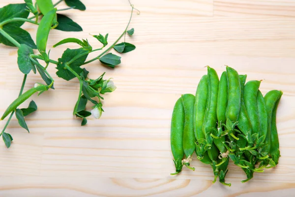 green peas in pods lies on a wooden background. Healthy green vegetables. Place for text.Delicious ripe green peas lying on a wooden table. Green pea  of top view on rustic wooden background with copy space, natural wooden table. Flat lay.