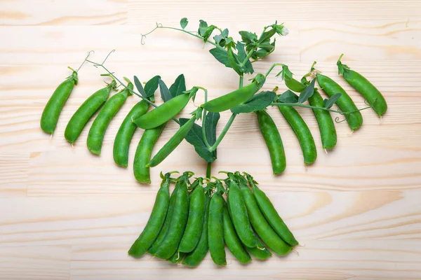 green peas in pods lies on a wooden background. Healthy green vegetables. Place for text.Delicious ripe green peas lying on a wooden table. Green pea  of top view on rustic wooden background with copy space, natural wooden table. Flat lay.