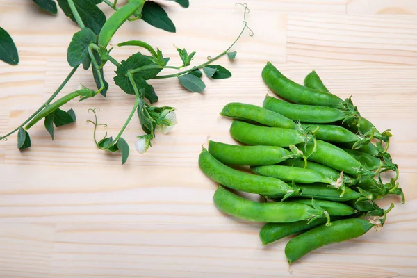 green peas in pods lies on a wooden background. Healthy green vegetables. Place for text.Delicious ripe green peas lying on a wooden table. Green pea  of top view on rustic wooden background with copy space, natural wooden table. Flat lay.