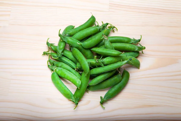 green peas in pods lies on a wooden background. Healthy green vegetables. Place for text.Delicious ripe green peas lying on a wooden table. Green pea  of top view on rustic wooden background with copy space, natural wooden table. Flat lay.