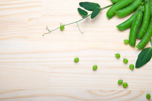 green peas in pods lies on a wooden background. Healthy green vegetables. Place for text.Delicious ripe green peas lying on a wooden table. Green pea  of top view on rustic wooden background with copy space, natural wooden table. Flat lay.